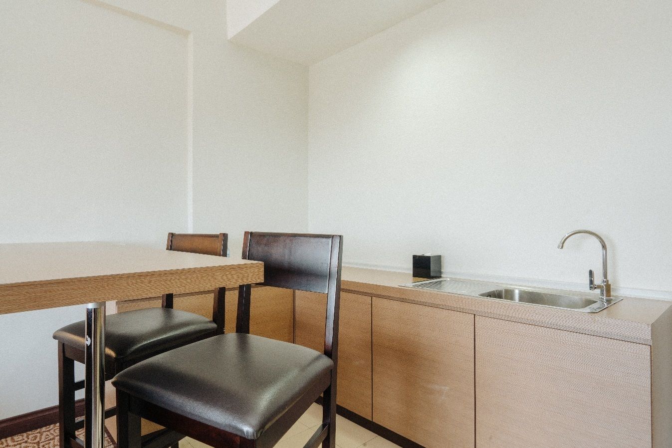 A compact kitchen with a wooden table and two chairs, a sink, and a small countertop.