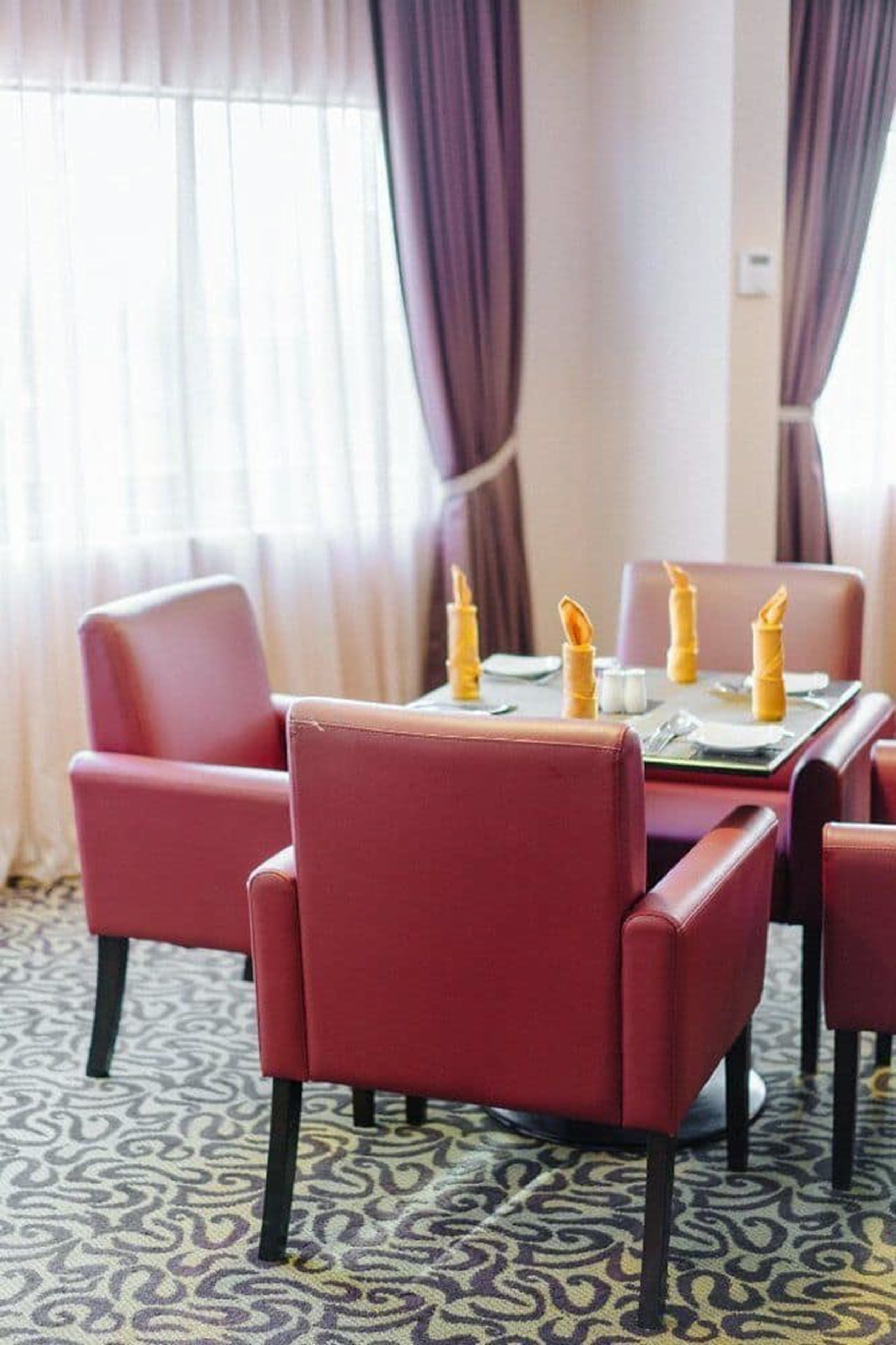 Een eetgedeelte met een tafel gedekt voor vier personen, omringd door rode fauteuils.