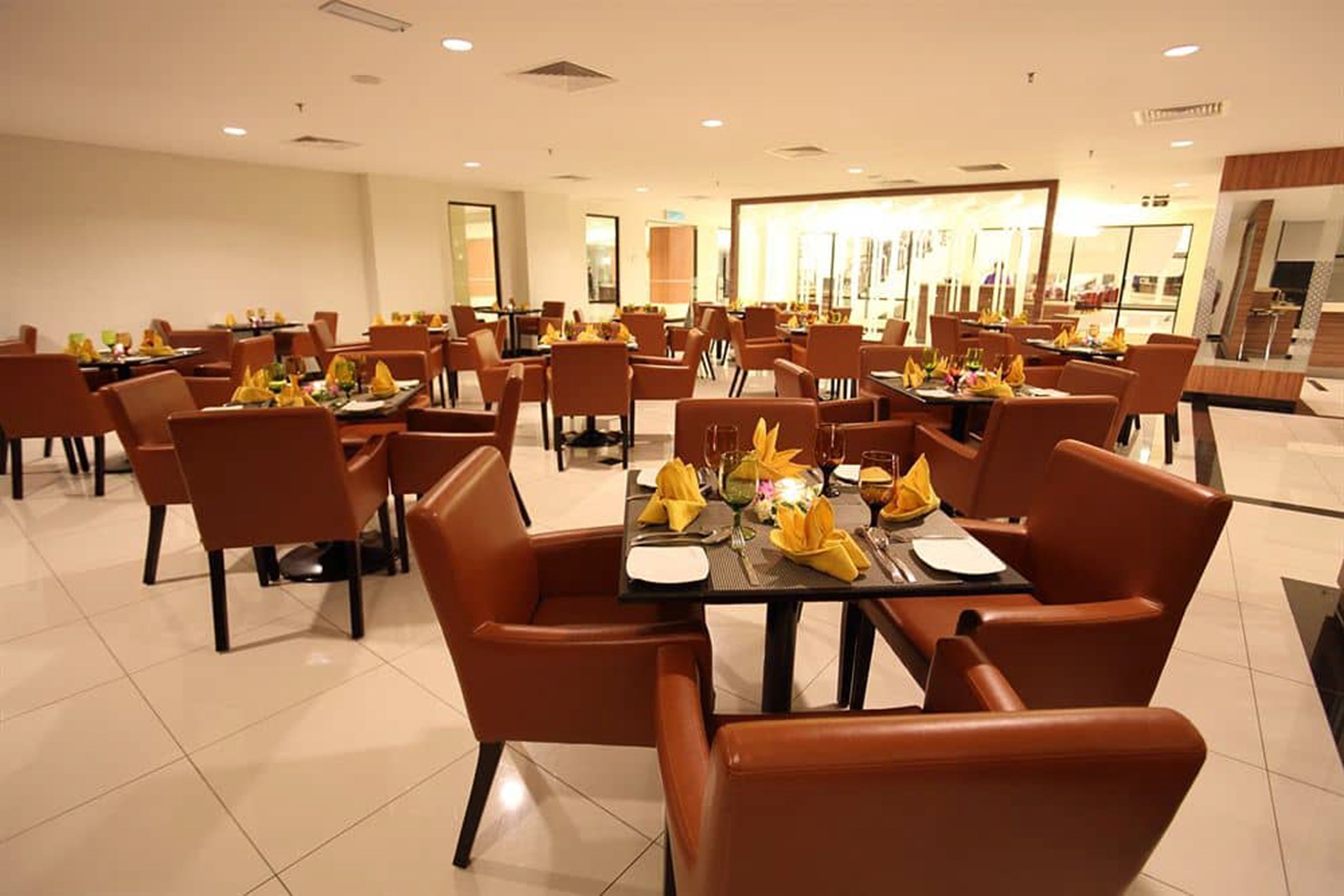 A spacious dining area with multiple tables and chairs, each set with yellow napkins and glassware.