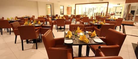 Un comedor amplio con varias mesas y sillas, cada conjunto con servilletas amarillas y cristalería.
