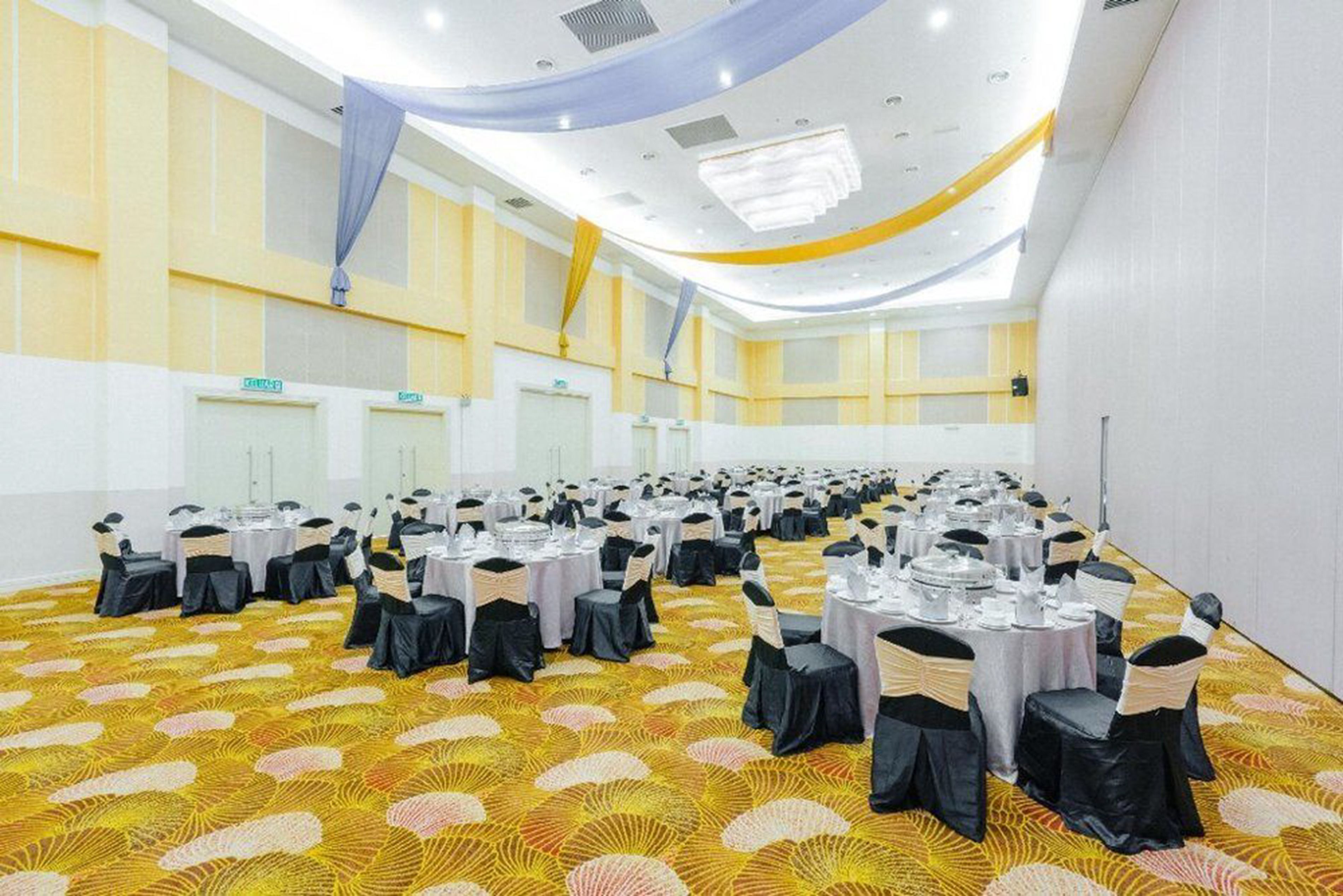 A large conference room with multiple round tables, each set with white tablecloths and black chairs.
