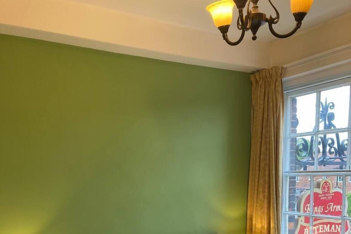 A hotel room with a bed, two bedside tables with lamps, a window with curtains, and a green wall.