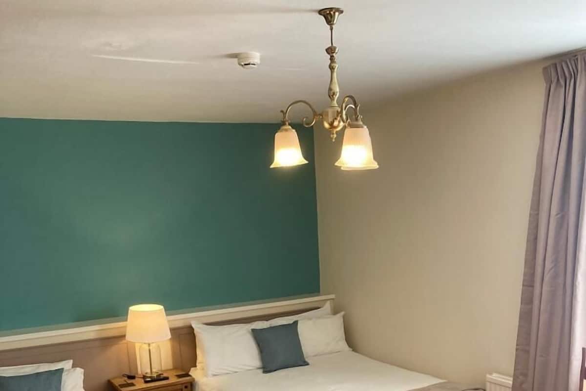 A hotel room with two beds, a nightstand with a lamp, a wooden table, and a red carpet.
