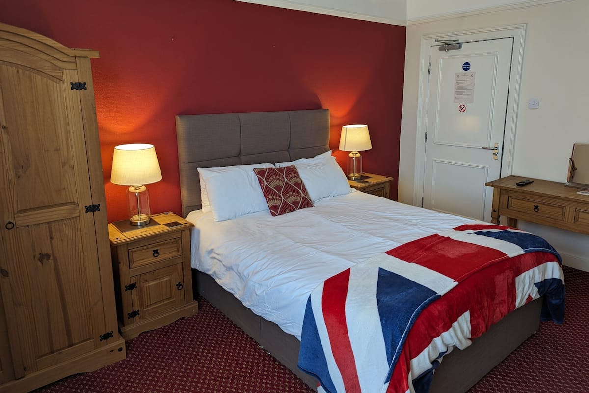 A neatly made bed with a red and white striped blanket, two bedside lamps, and a wooden wardrobe.