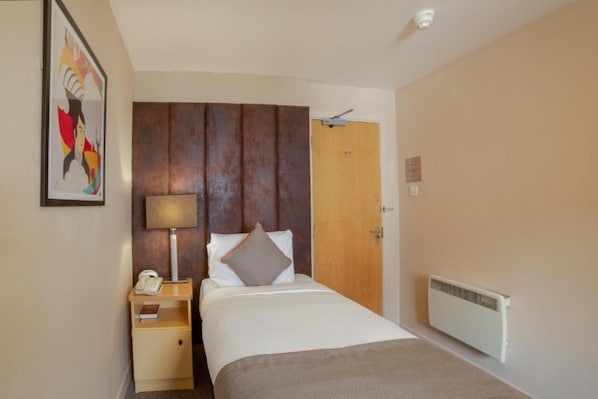 Une chambre d’hôtel avec un lit, une table de chevet avec une lampe, un téléphone, un radiateur et une porte.