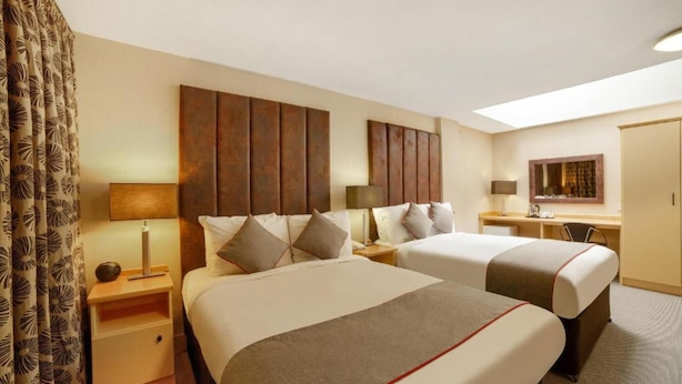 Une chambre d’hôtel avec deux lits, un bureau, une chaise et une armoire.