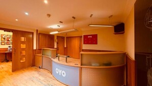 Un espace d’accueil avec un comptoir incurvé portant l’inscription « OYO », des portes en bois et un téléviseur fixé au mur.
