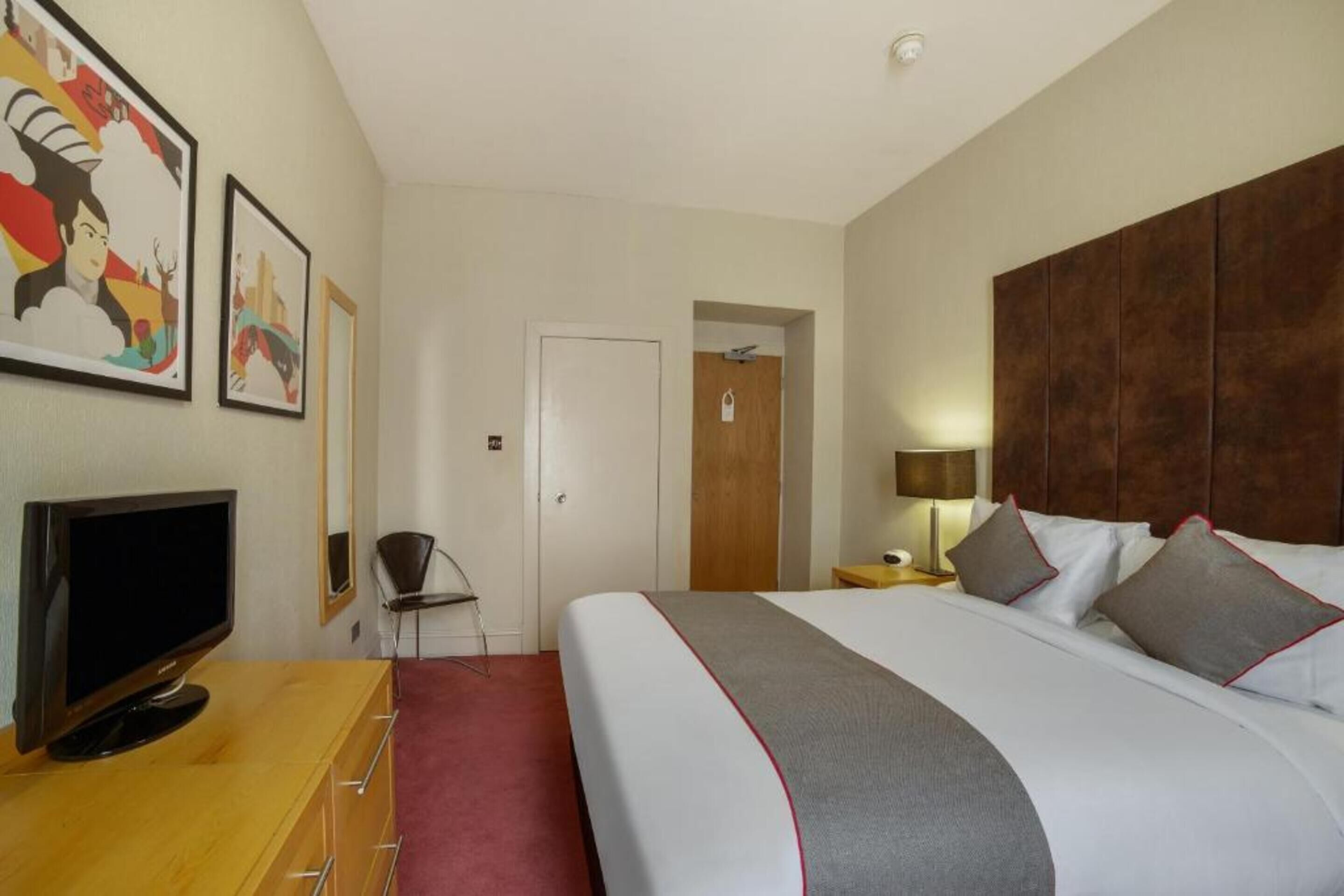 A hotel room with a large bed, a TV, a desk, and a chair.