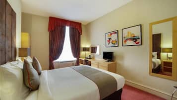 A hotel room with a bed, a desk, a chair, a TV, and artwork on the walls.