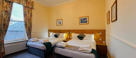 A hotel room with two beds, a large window with curtains, and a radiator.