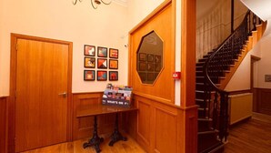 Un couloir en bois avec un escalier, un mur orné de tableaux encadrés et une table sur laquelle se trouve un présentoir à magazines intitulé « À l’affiche ».