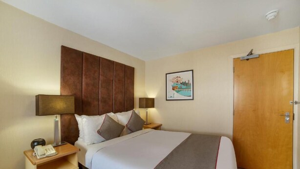 A hotel room with a bed, nightstands, a telephone, a lamp, a door, and a wall-mounted picture. - Highland Aberdeen City Centre (Aberdeen)