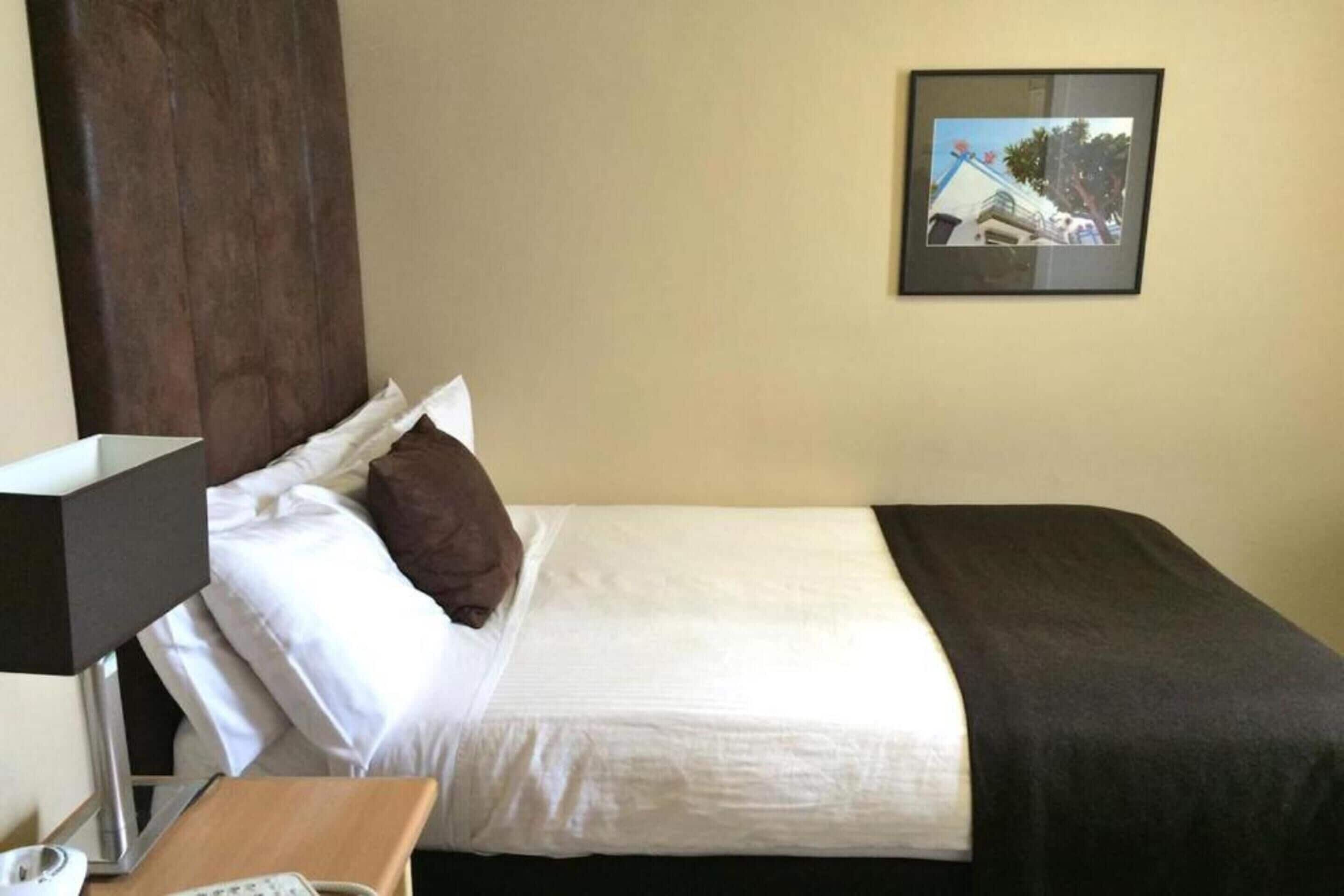 A hotel room with a bed, a nightstand, a lamp, and a framed picture on the wall.