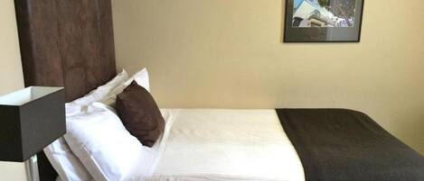 A hotel room with a bed, a nightstand, a lamp, and a framed picture on the wall.