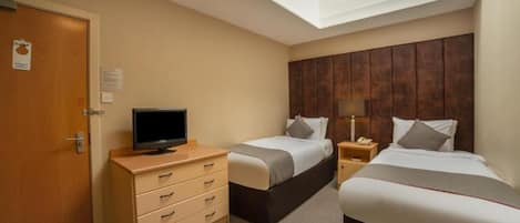 A hotel room with two beds, a TV on a dresser, a wooden headboard, and a skylight.