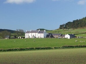A large white building with multiple smaller structures in a rural setting. - Knockaloe Beg Farm (Glenmaye)