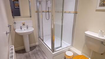 Une salle de bain moderne avec une douche à parois de verre, un lavabo sur colonne et des toilettes avec un abattant en bois.