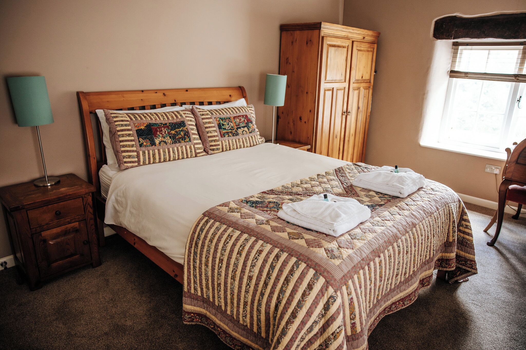 A neatly made bed with a patterned quilt, two pillows, and two folded towels on the bed.