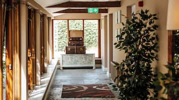 A hallway with a reception desk, a green exit sign, and a potted plant.