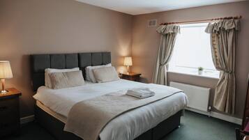 Una habitación de hotel con cama, lámparas de noche, una ventana con cortinas y un radiador.