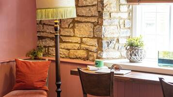 Una habitación acogedora con pared de piedra, una mesa de madera, una lámpara y una ventana con persianas.