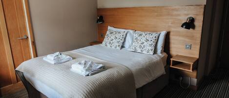 A hotel room with a bed, two bedside tables, a nightstand, and a door.