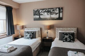 Habitación de hotel con dos camas, cada una con cabecero, mesitas de noche, lámparas y almohadas decorativas.