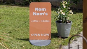 A sign for 'Nom Nom's' coffee and nibble sign in front of a stone building with a window. - Northover Manor Hotel (Yeovil)