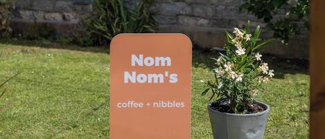 Letrero de 'Nom Nom's' para café y bocadillos frente a un edificio de piedra con ventana.
