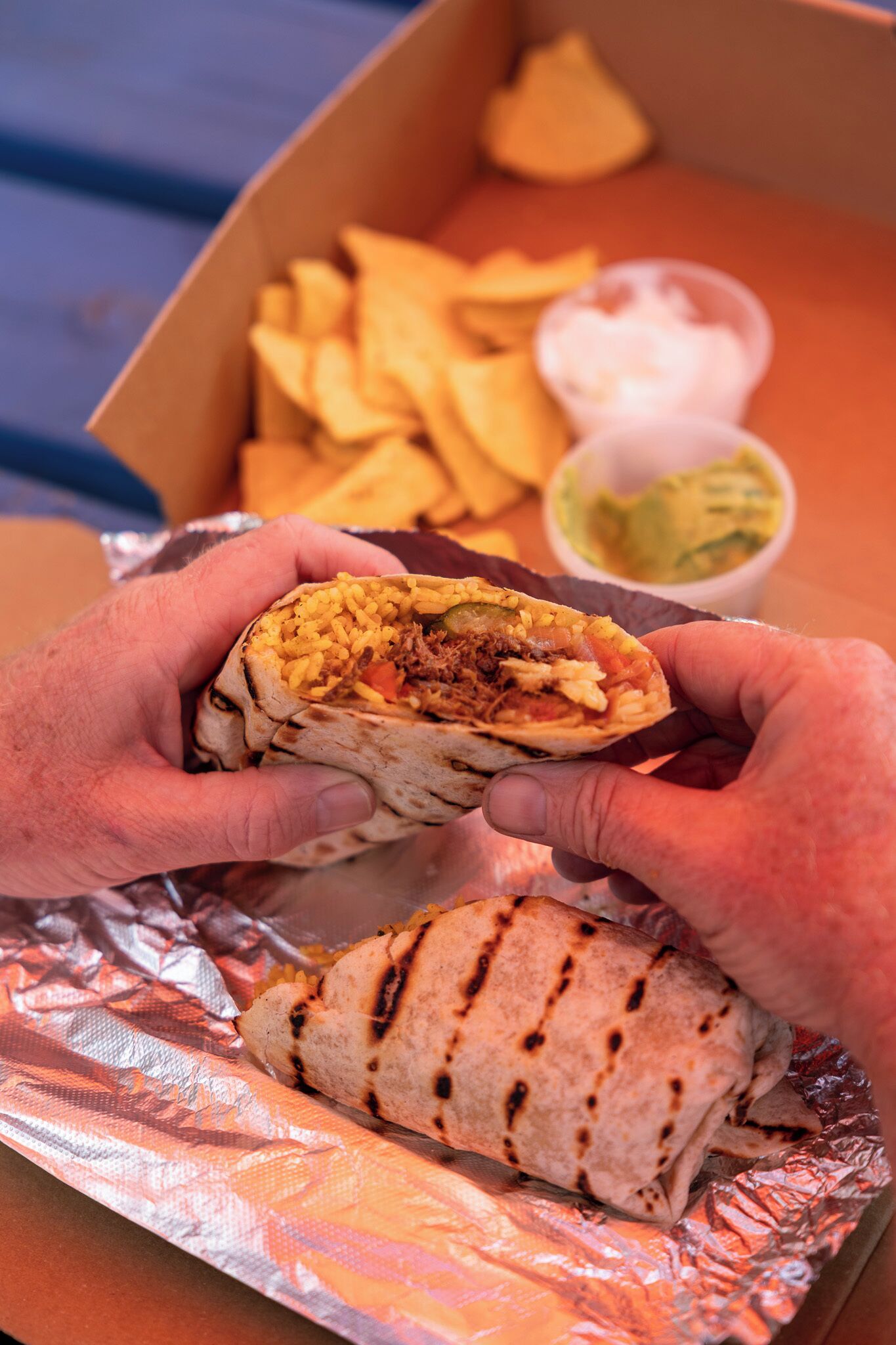 Un burrito con relleno visible, envuelto en papel de aluminio, y una porción de papas fritas en una caja.