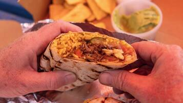 Un burrito con relleno visible, envuelto en papel de aluminio, y una porción de papas fritas en una caja.