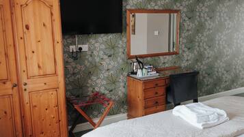 A hotel room with a bed, a wooden wardrobe, a desk with a chair, a flat-screen TV, and a mirror.