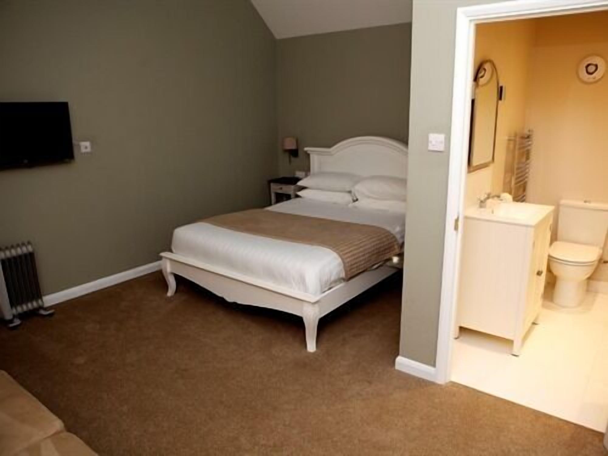 Une chambre à coucher comprenant un lit, une table de chevet, une commode, un radiateur et une salle de bain avec des toilettes et un lavabo.