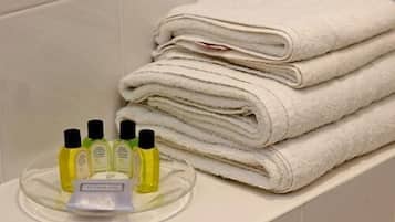 Un baño con una pila de toallas blancas en un estante y una bandeja con artículos de aseo, incluyendo botellas y dispensador de jabón.