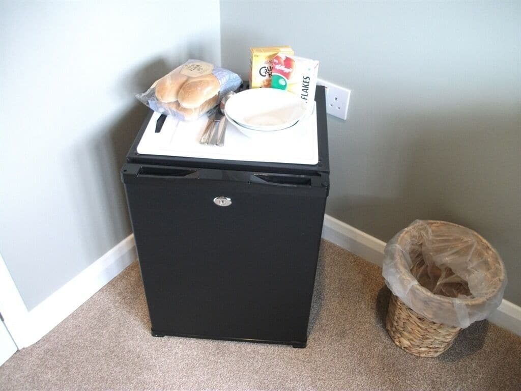 A black refrigerator with a freezer compartment, a microwave, and a small sink. There is a trash can and a basket next to the refrigerator.