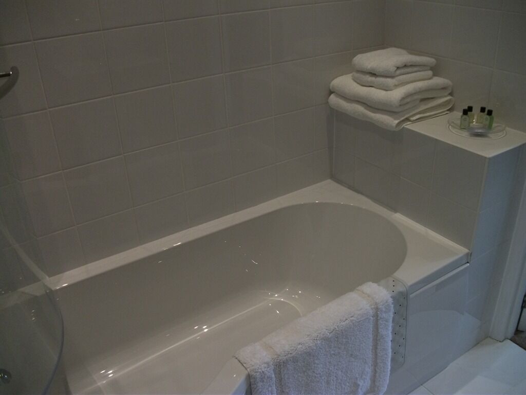 Un baño con bañera, una pila de toallas blancas y un estante con artículos de aseo.