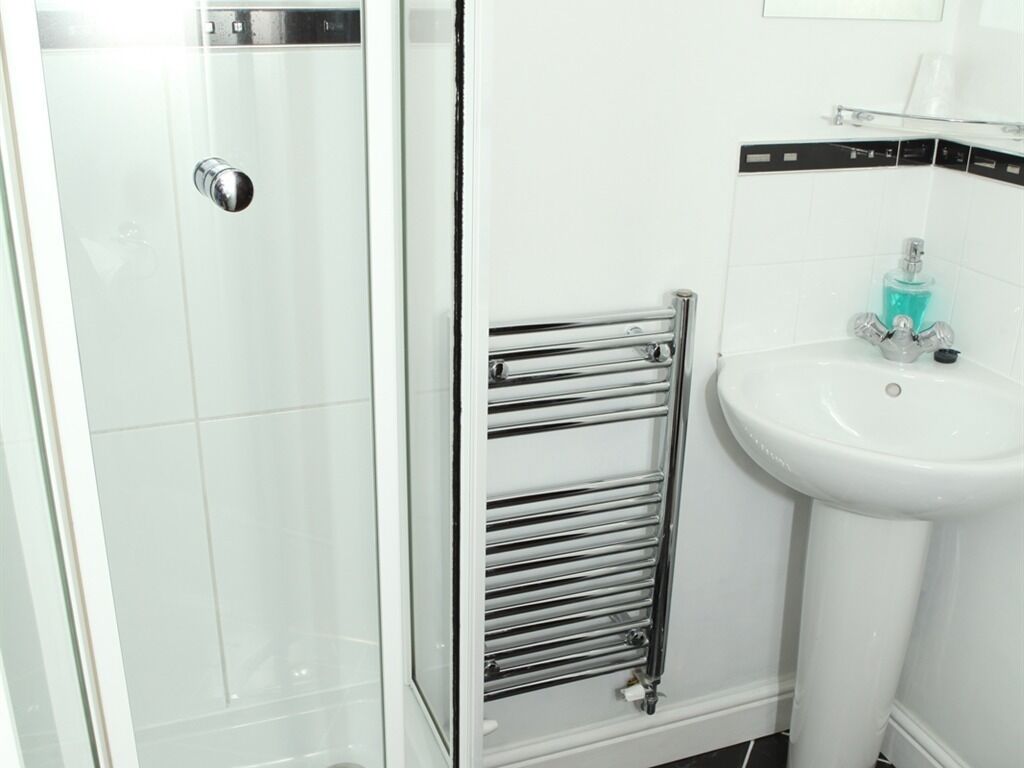 A bathroom with a glass shower enclosure, a chrome towel rack, and a white sink with a soap dispenser.