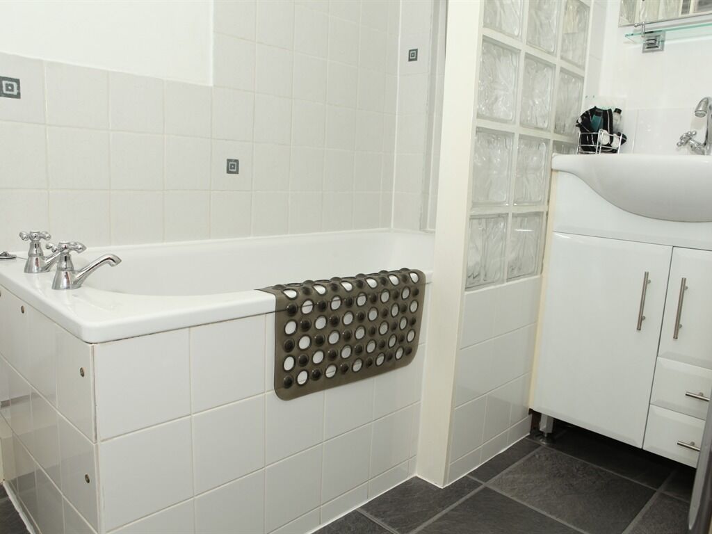 A bathroom with white tiles, a bathtub, a towel rack, and a sink with cabinets.