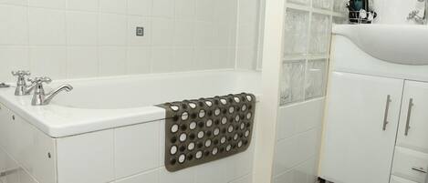 Ein Badezimmer mit weißen Fliesen, einer Badewanne, einem Handtuchhalter und einem Waschbecken mit Schränken.