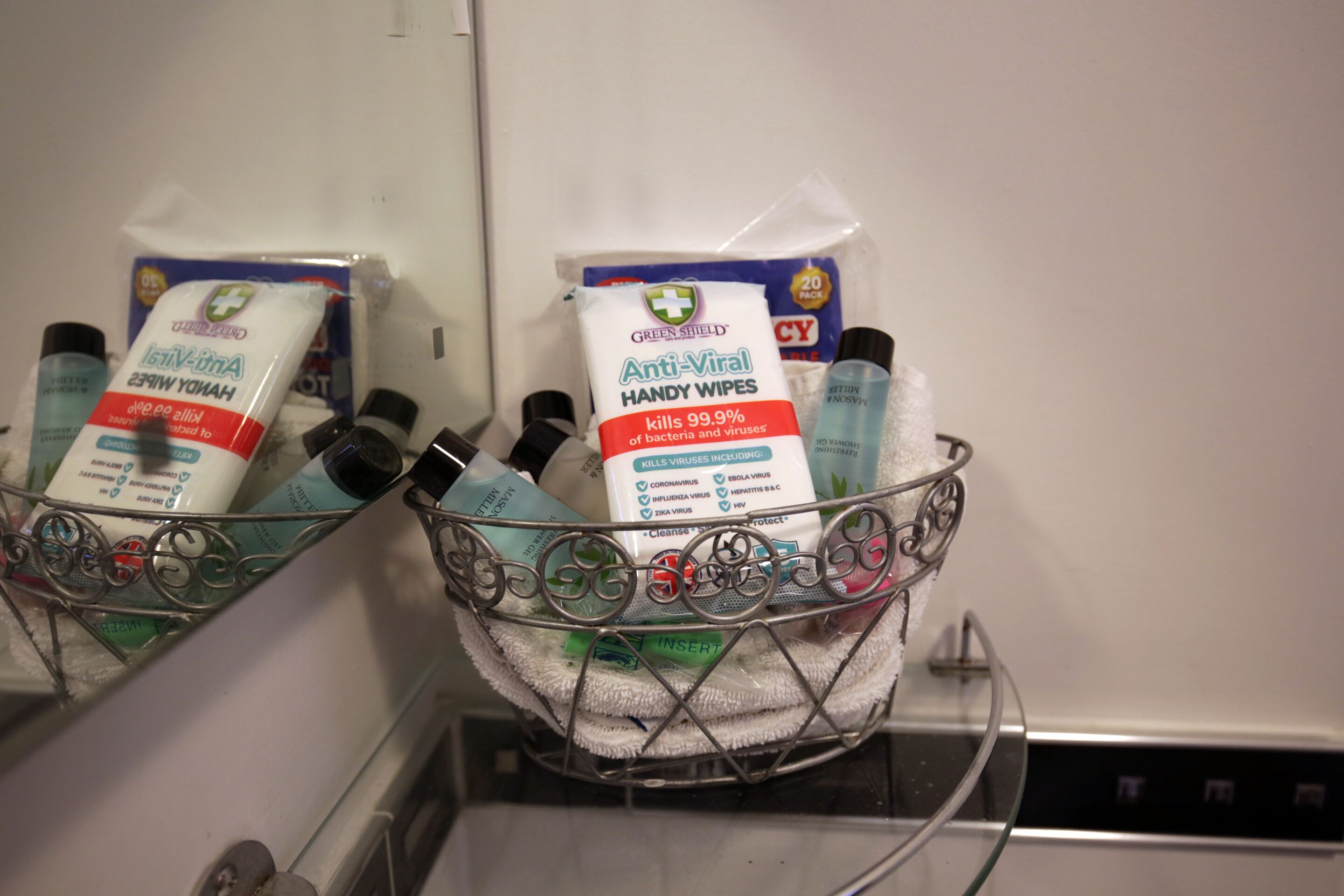 A metal basket containing various hygiene products including hand sanitizer, anti-viral hand wipes, and a bottle of hand soap.