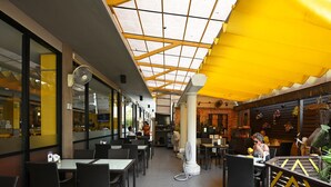 Een terrasrestaurant met rieten meubels, een geel zonnescherm en een glazen dak.