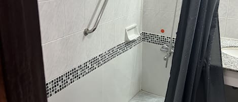Baño con paredes de azulejos blancos, zona de ducha y barandilla.
