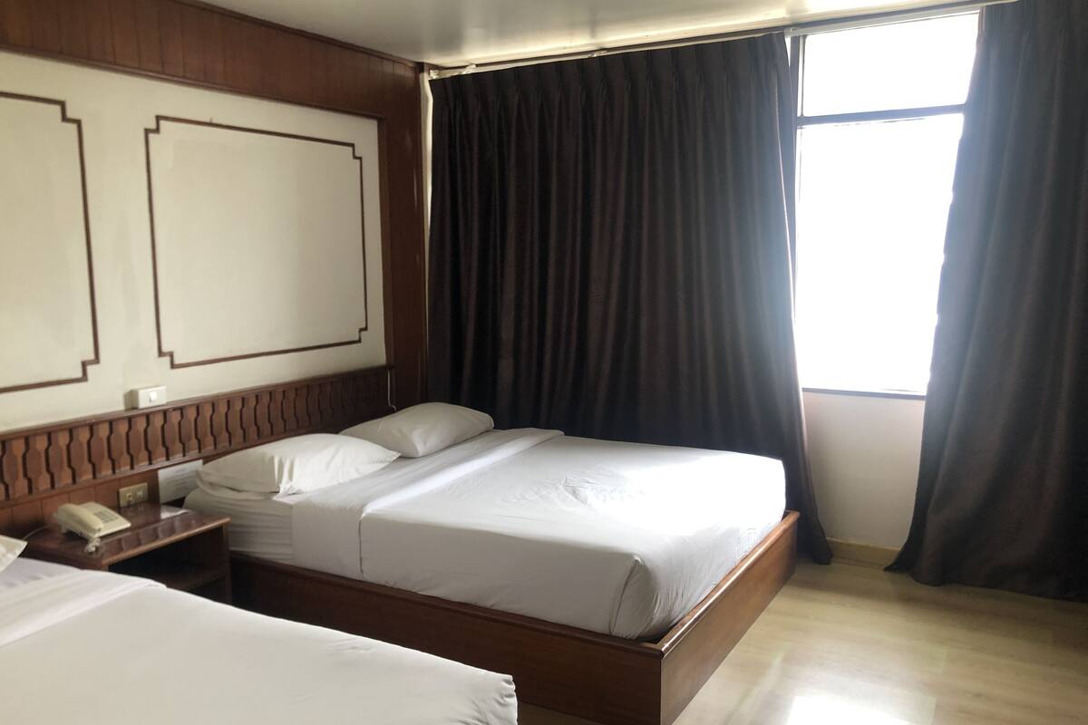 Ein Hotelzimmer mit einem Doppelbett, einem Nachttisch mit Telefon und einem Fenster mit Verdunkelungsvorhängen.