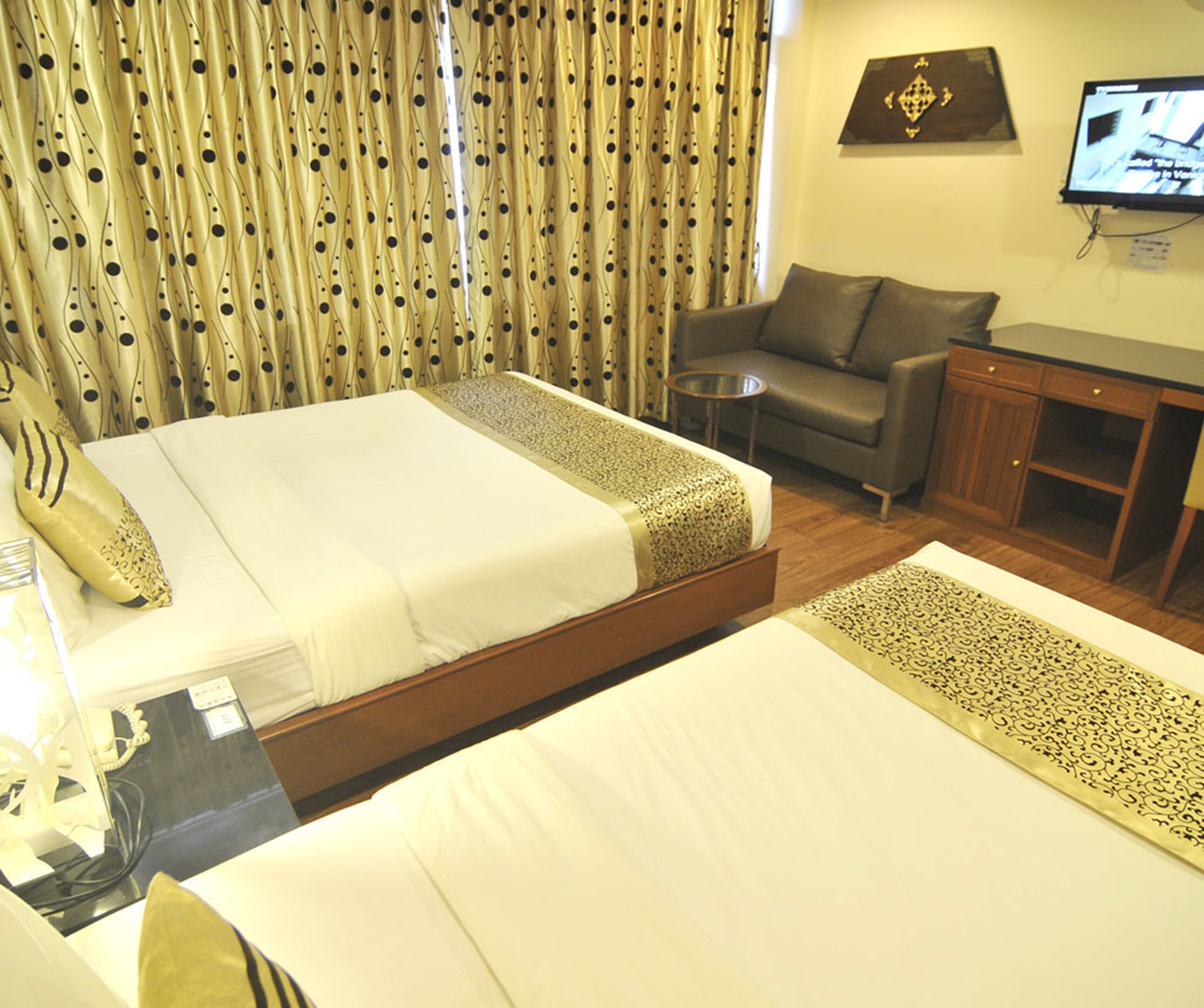 A hotel room with two beds, a sofa, a TV, and a desk.