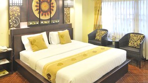 Hotelkamer met een groot bed, een hoofdbord met decoratieve panelen, een kleine tafel met stoelen en een raam met gordijnen.
