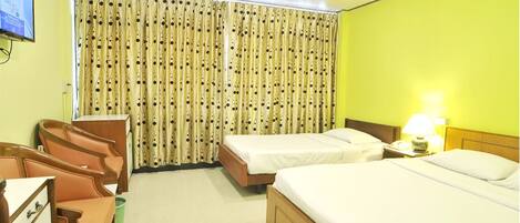 A hotel room with two single beds, a desk with a chair, a television, and curtains with a polka dot pattern.
