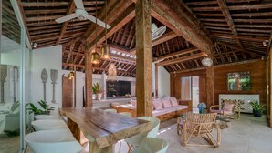 A spacious room with a wooden ceiling, a large dining table, and modern seating. - Villa Saffira (Seminyak)