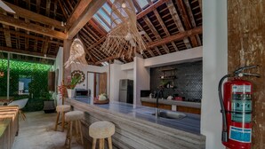 A modern kitchen with a marble countertop, wooden stools, a fire extinguisher, and a green wall. - Villa Saffira (Seminyak)