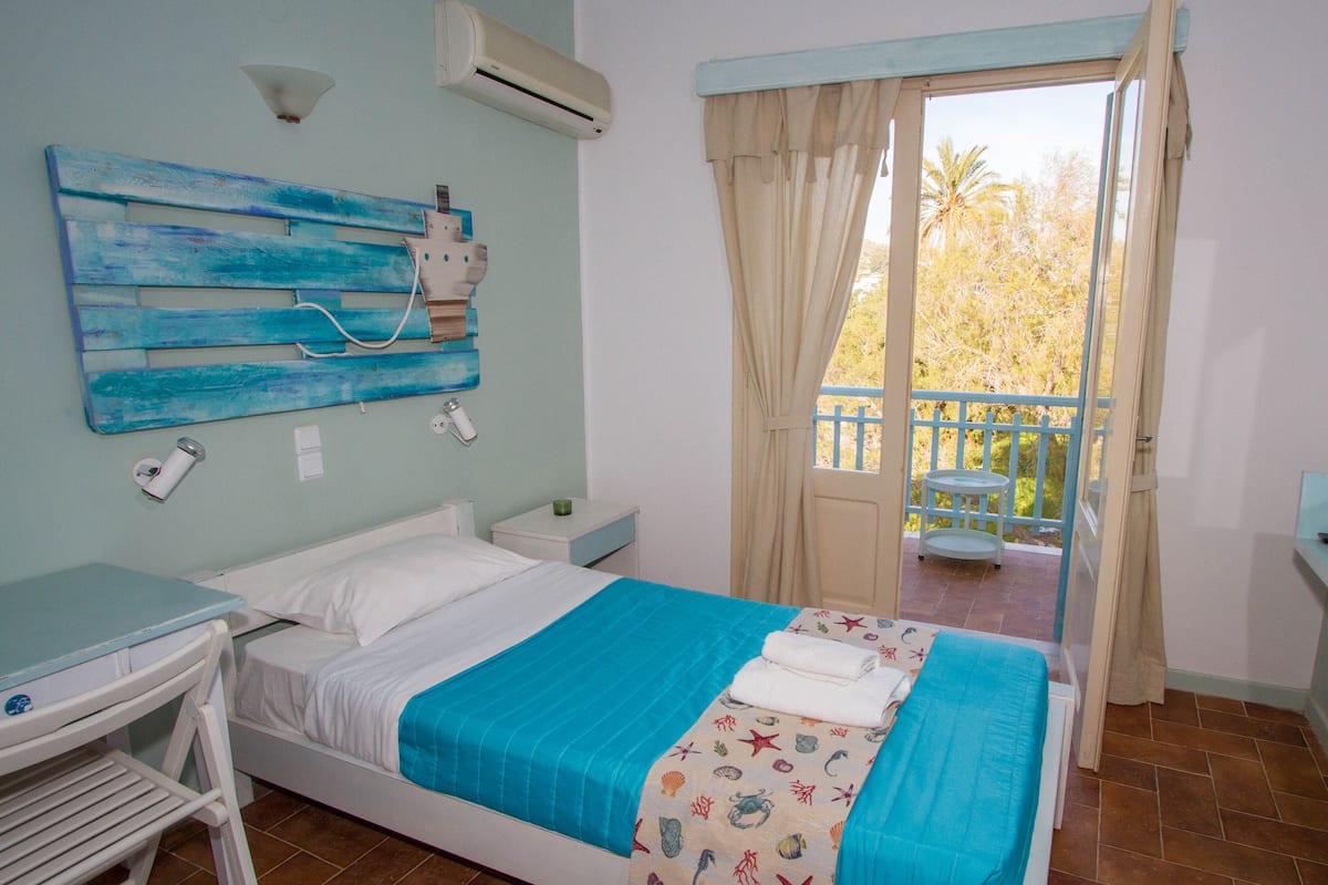 A bedroom with a bed, a desk, a chair, a window with curtains, and a balcony with a table and chair.