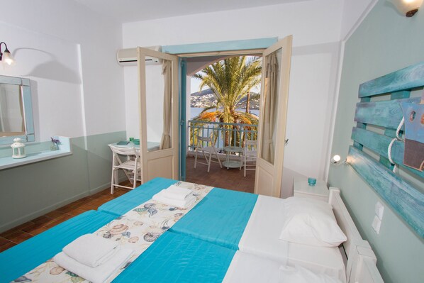 Un dormitorio con cama, ventana, mesita de noche y vista a un balcón con sillas y una palmera.
